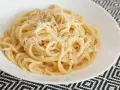 Pyszne spaghetti carbonara przepis na talerzu, posypane parmezanem i świeżo mielonym pieprzem.