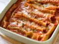 Pyszne cannelloni ze szpinakiem zapieczone w sosie pomidorowym, posypane serem i ziołami.