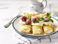 Pyszne naleśniki z serem, udekorowane bitą śmietaną, malinami i miętą, gotowe do podania.