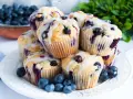 Stos pysznych muffinek z borówkami, polanych lukrem, ozdobionych świeżymi borówkami. Idealne na śniadanie lub deser.