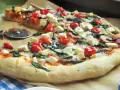 Pyszna pizza ze szpinakiem, pomidorkami koktajlowymi i kostkami sera feta. Idealna na szybki obiad.