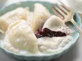 Pyszne pierogi z jagodami, polane śmietaną, w niebieskiej miseczce. Widoczny widelec.