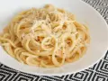 Pyszna carbonara bez śmietany, z parmezanem i pieprzem, podana w białej misce na wzorzystym obrusie.