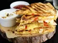 Stos pysznych kawałków quesadilli z kurczakiem, roztopionym serem i papryką, podane z dipami.