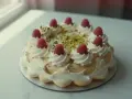 Wykwintny tort pistacjowo malinowy, ozdobiony bitą śmietaną, malinami i posypką z pistacji.