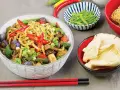 Pyszny makaron chow mein z warzywami i papryczkami chili, obok miseczki z grzybami i fasolką.