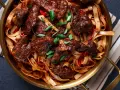 Pyszne wolowina po seczuańsku z makaronem, papryczkami chili i szczypiorkiem w złotej misie.