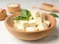 Kostki tofu w drewnianej misce z bazylią. Czy tofu można jeść na surowo? Tak, to świetna baza do sałatek i przekąsek.