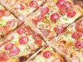 Kawałki pysznej pizzy na cienkim cieście z kiełbasą i serem, posypane ziołami.