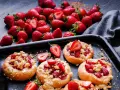 Pyszne drożdżówki z truskawkami i kruszonką, obok świeże owoce.