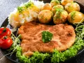 Idealny sznycel a schabowy na talerzu: złocisty, chrupiący kotlet z ziemniaczkami, surówką i pomidorkami.
