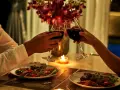 Romantyczna kolacja dla dwojga przy świecach. Dwie pary kieliszków z czerwonym winem unoszą się w geście toastu.