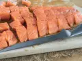 Świeży, pokrojony łosoś do sushi, doprawiony, leży na desce obok noża. Idealny łosoś do sushi.
