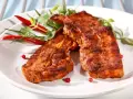 Dwa soczyste kawałki boczku na grilla, przyprawione i ozdobione papryczkami chili i zielonymi listkami.