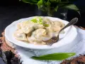 Pyszne pierogi ze szpinakiem i serem, udekorowane czosnkiem niedźwiedzim, na białym talerzu.