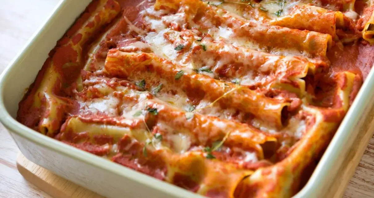 Pyszne cannelloni ze szpinakiem zapieczone w sosie pomidorowym, posypane serem i ziołami.