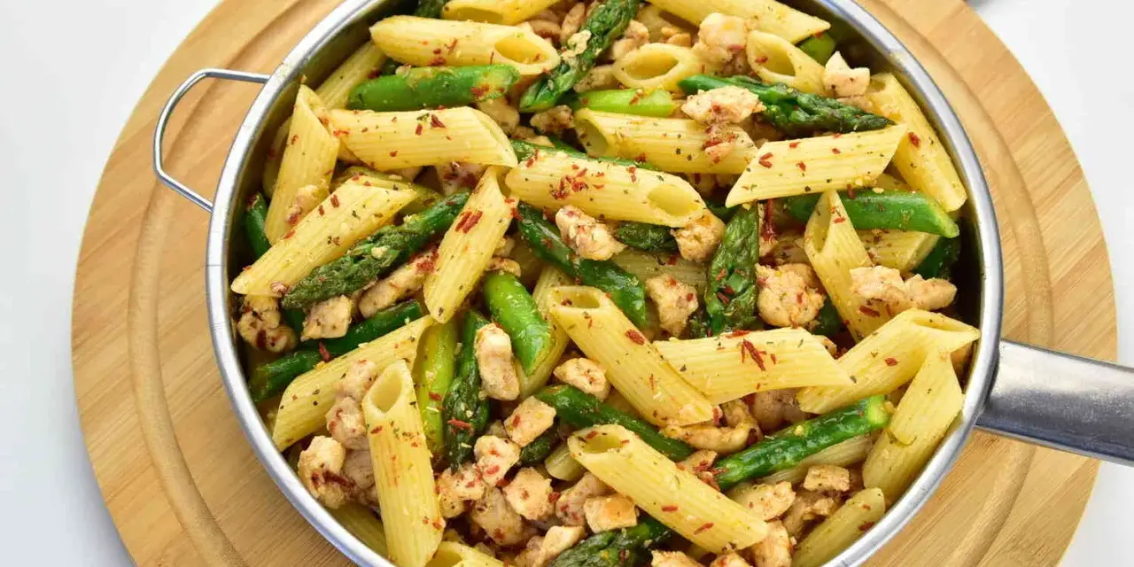 Penne z kurczakiem i szparagami, posypane papryką. Pyszne danie na obiad.