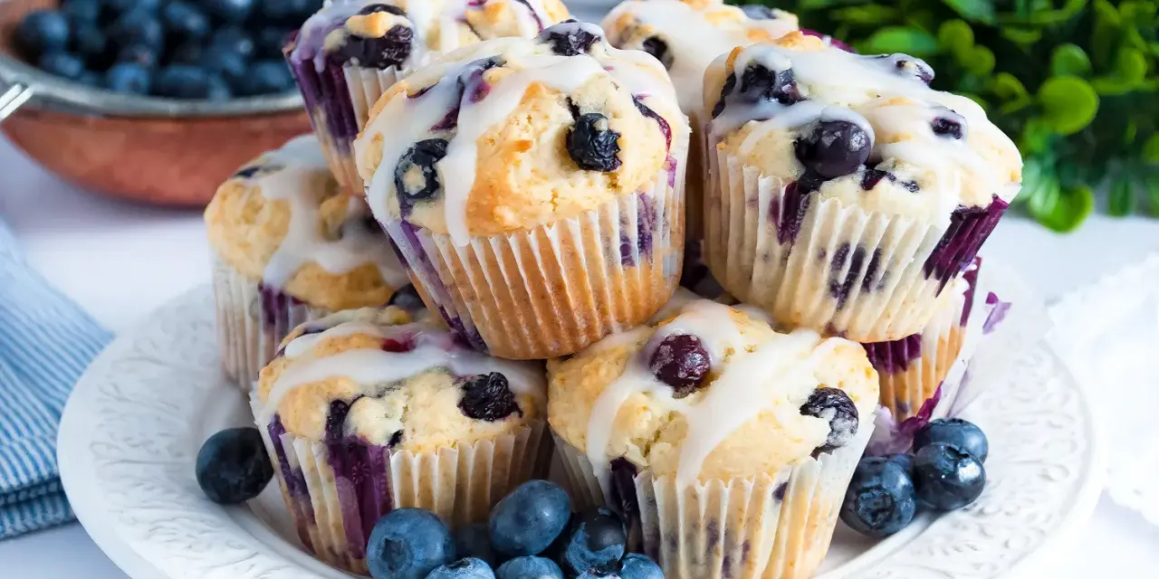 Stos pysznych muffinek z borówkami, polanych lukrem, ozdobionych świeżymi borówkami. Idealne na śniadanie lub deser.