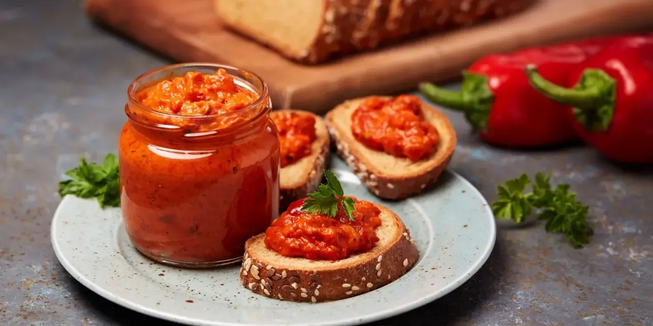Słoik ajvaru i pieczywo z pastą. Ajvar do czego? Idealny na kanapki, dodatek do mięs i warzyw.