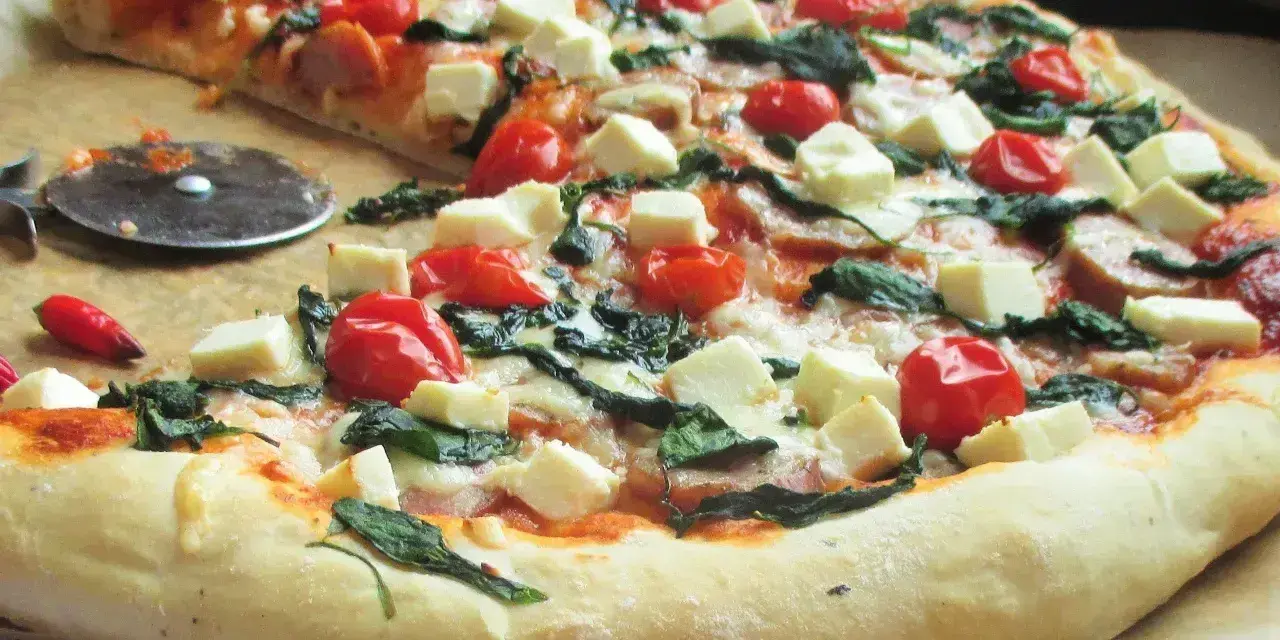 Pyszna pizza ze szpinakiem, pomidorkami koktajlowymi i kostkami sera feta. Idealna na szybki obiad.