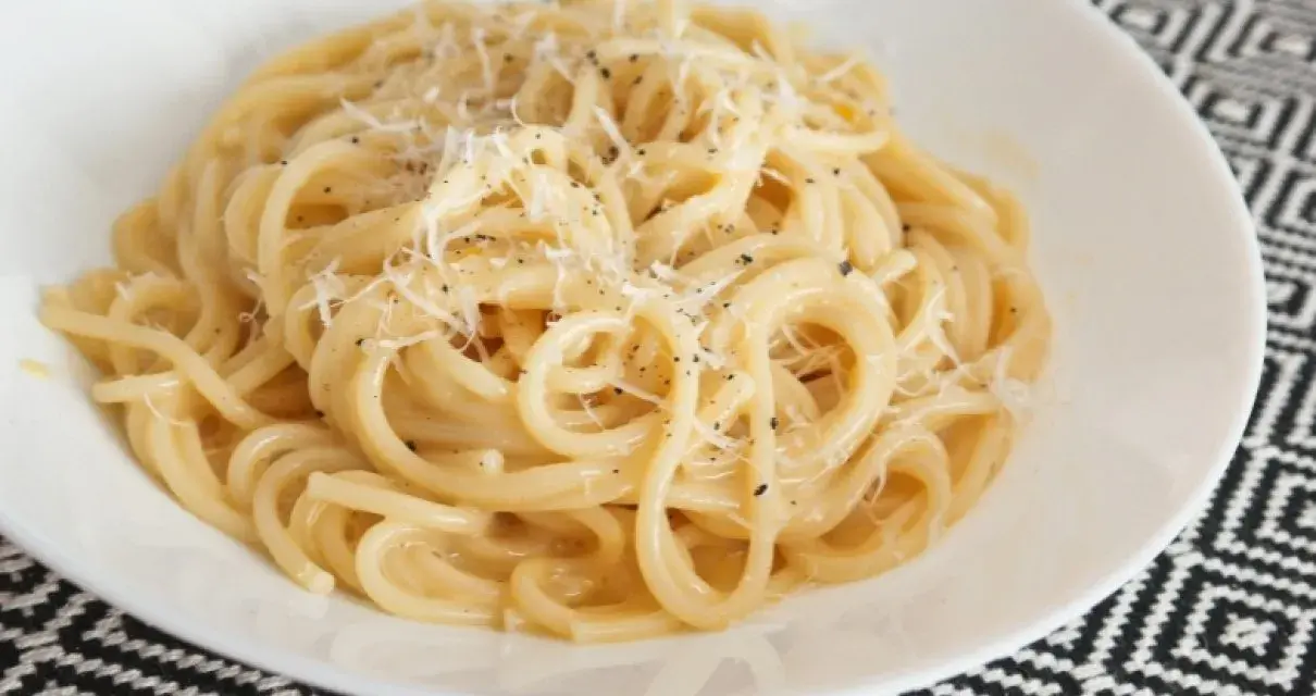 Pyszna carbonara bez śmietany, z parmezanem i pieprzem, podana w białej misce na wzorzystym obrusie.