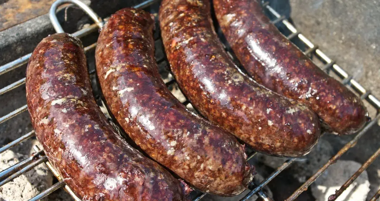 Cztery soczyste kaszanki z grilla pieką się na ruszcie, uwalniając apetyczny aromat.