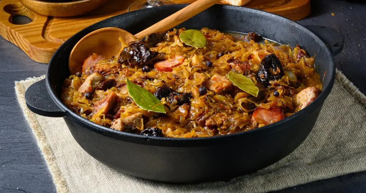 Pyszny bigos w żeliwnym naczyniu, z widocznymi kawałkami mięsa, śliwkami i liśćmi laurowymi. Idealne danie, gdy zastanawiasz się, jakie mięso do bigosu wybrać.