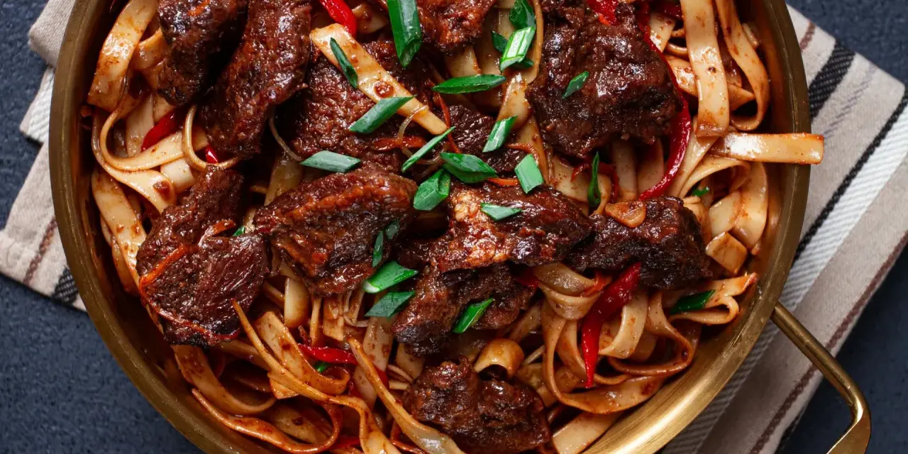 Pyszne wolowina po seczuańsku z makaronem, papryczkami chili i szczypiorkiem w złotej misie.