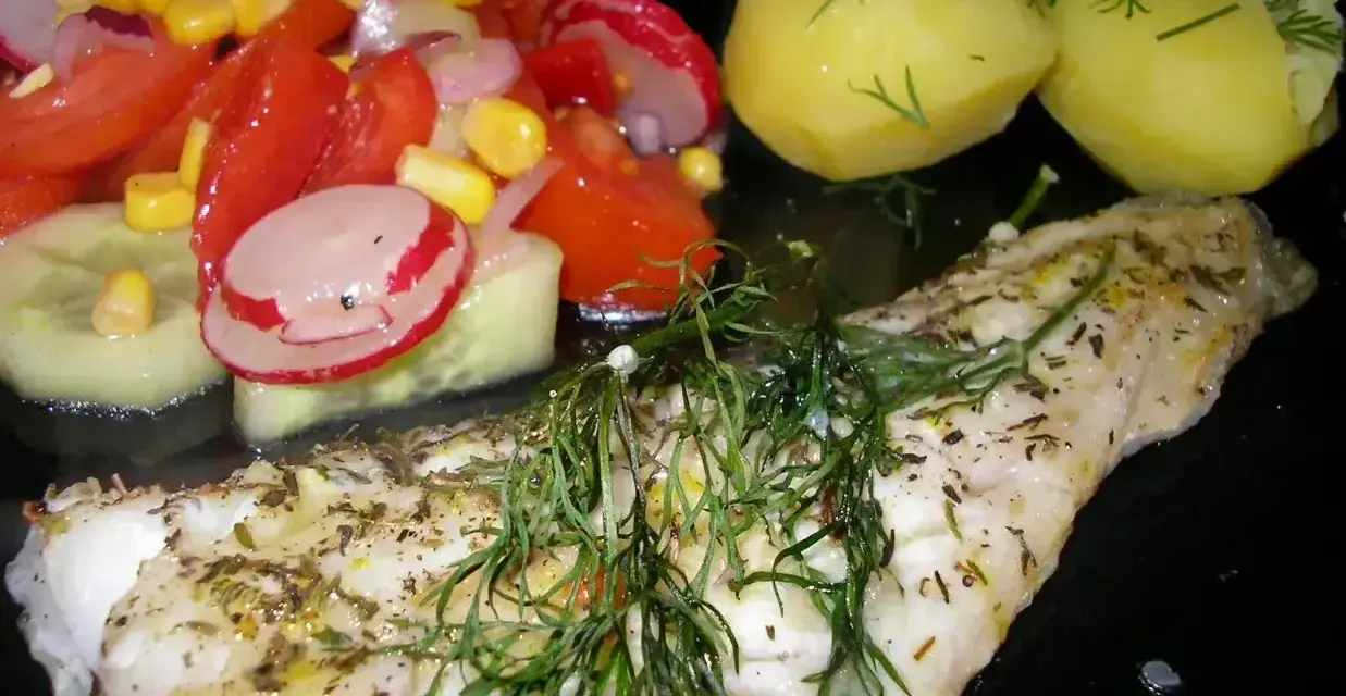 Pyszny mintaj z piekarnika, podany z ziemniakami i świeżą sałatką z pomidorów, ogórka i rzodkiewki.