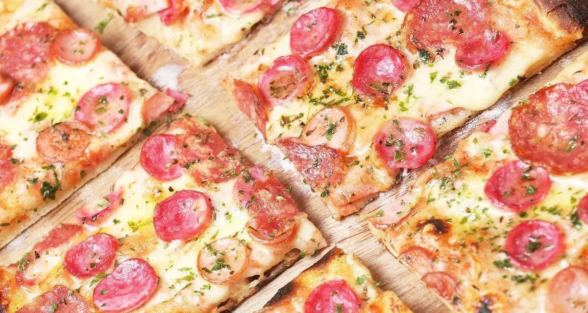 Kawałki pysznej pizzy na cienkim cieście z kiełbasą i serem, posypane ziołami.
