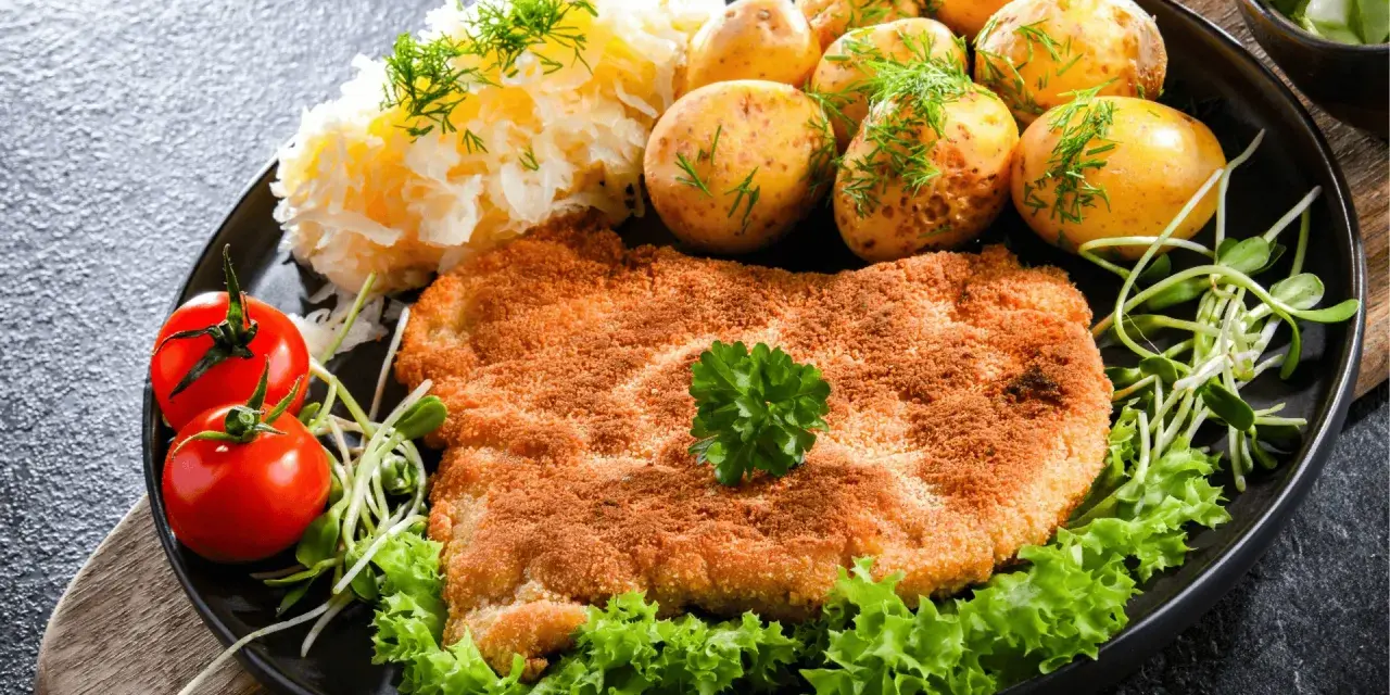 Idealny sznycel a schabowy na talerzu: złocisty, chrupiący kotlet z ziemniaczkami, surówką i pomidorkami.