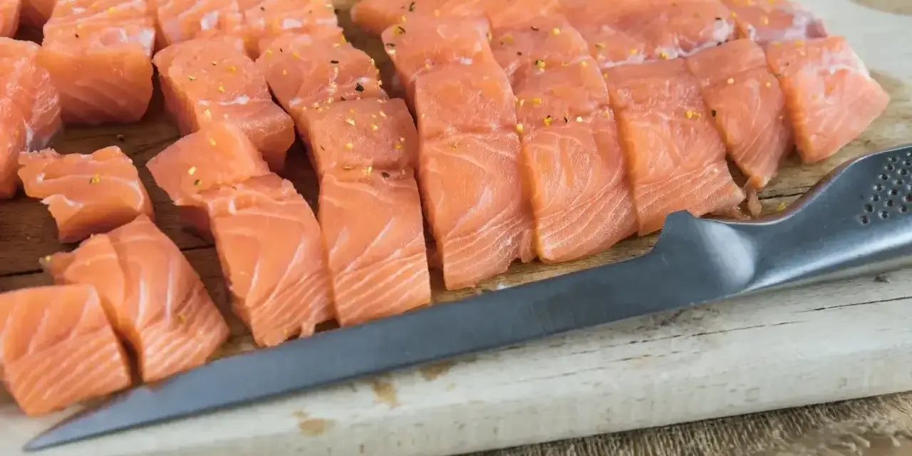 Świeży, pokrojony łosoś do sushi, doprawiony, leży na desce obok noża. Idealny łosoś do sushi.