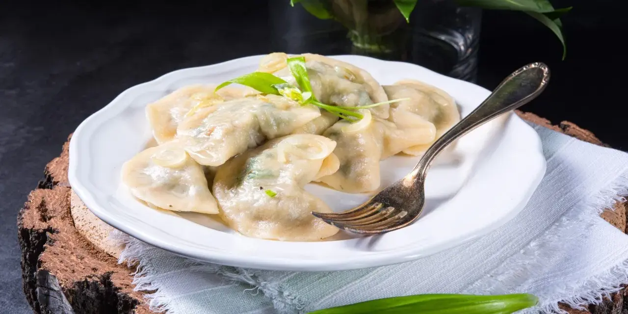 Pyszne pierogi ze szpinakiem i serem, udekorowane czosnkiem niedźwiedzim, na białym talerzu.
