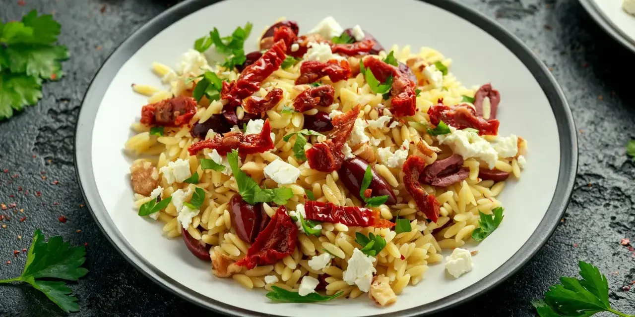 Pyszna sałatka z makaronem orzo, z suszonymi pomidorami, oliwkami, fetą i natką pietruszki.