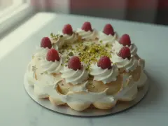Wykwintny tort pistacjowo malinowy, ozdobiony bitą śmietaną, malinami i posypką z pistacji.