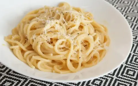 Pyszne spaghetti carbonara przepis na talerzu, posypane parmezanem i świeżo mielonym pieprzem.