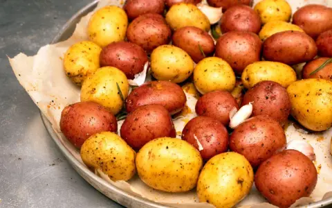 Ziemniaki z ogniska, czerwone i żółte, przyprawione czosnkiem i ziołami, gotowe do pieczenia.