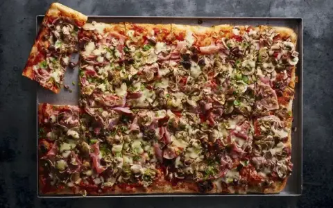 Pyszna pizza domowa przepis na blachę z szynką, pieczarkami i oliwkami. Idealna na rodzinne spotkanie.