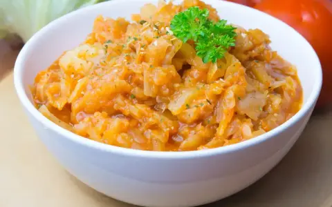Pyszny bigos ze słodkiej kapusty, duszony z pomidorami i przyprawami, udekorowany natką pietruszki.