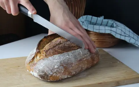 Ręka kroi pyszny, świeżo upieczony chleb z garnka. Chrupiąca skórka i miękki środek zachęcają do spróbowania.
