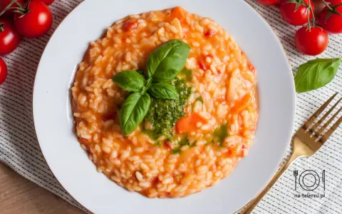 Pyszne risotto z pomidorami, udekorowane bazylią i pesto, czeka na talerzu. Obok świeże pomidorki i złoty widelec.