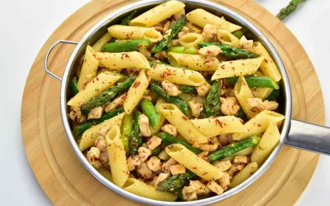 Penne z kurczakiem i szparagami, posypane papryką. Pyszne danie na obiad.