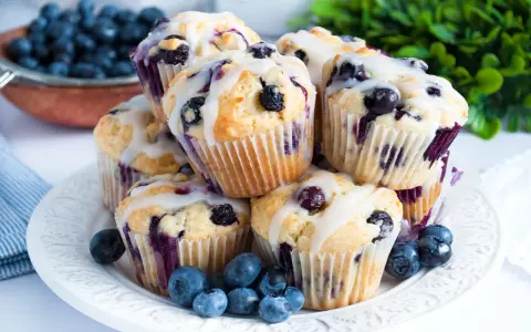 Stos pysznych muffinek z borówkami, polanych lukrem, ozdobionych świeżymi borówkami. Idealne na śniadanie lub deser.