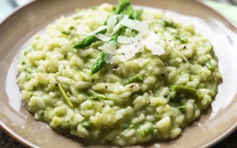 Kremowe risotto ze szparagami, posypane płatkami parmezanu i świeżo mielonym pieprzem.