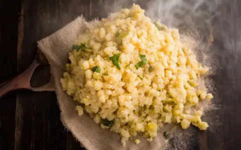 Gorąca kasza bulgur gotowanie na drewnianym stole, parująca i ozdobiona zielonymi ziołami.