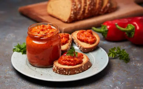 Słoik ajvaru i pieczywo z pastą. Ajvar do czego? Idealny na kanapki, dodatek do mięs i warzyw.