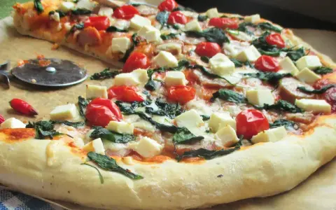 Pyszna pizza ze szpinakiem, pomidorkami koktajlowymi i kostkami sera feta. Idealna na szybki obiad.
