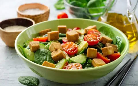 Kolorowa sałatka z chrupiącym tofu, pomidorkami koktajlowymi i ogórkiem na świeżym szpinaku.