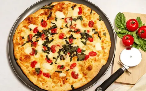 Pyszna pizza z serka wiejskiego, pomidorkami koktajlowymi i bazylią. Obok leży krajalnica do pizzy i świeże pomidory.