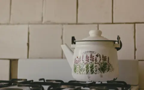 Biały czajnik z emaliowanym motywem lawendy i pszczół, stojący na kuchence. Emalia co to? To trwałe, szklane pokrycie naczyń.
